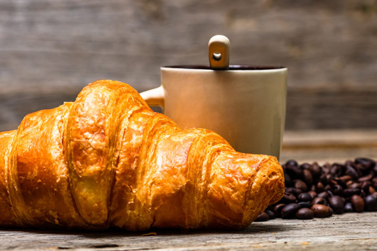 A closeup shot of freshly baked golden brown French croissant with coffee