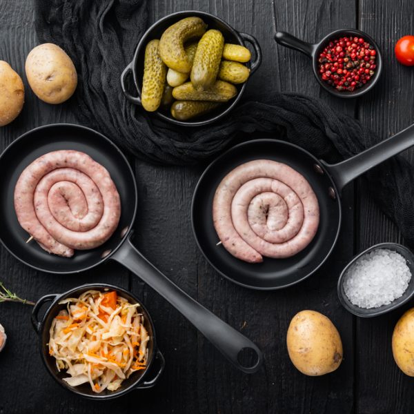 Wurst or Bratwurst with Fermented Cabbage, Pickled Cucumber, and Spices in cast iron frying pan, on black wooden table background, top view flat lay