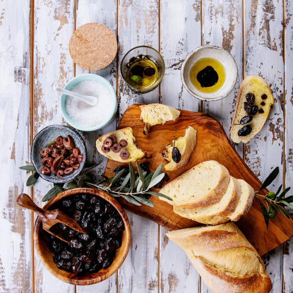 Traditional Greek Appetizer olives with bread, olive oil and balsamic vinegar served on rustic olive wooden board over a white wooden background. Top View