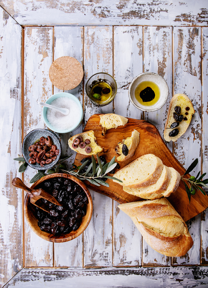 Traditional Greek Appetizer olives with bread, olive oil and balsamic vinegar served on rustic olive wooden board over a white wooden background. Top View