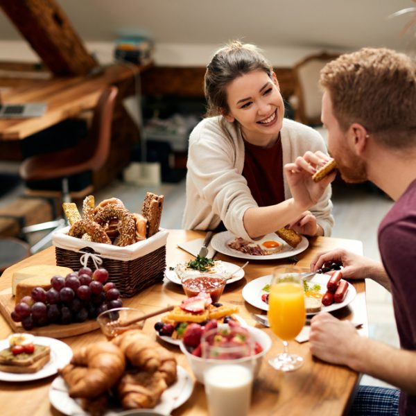 Happy couple enjoying in breakfast together at home. Focus is on woman feeding her boyfriend.