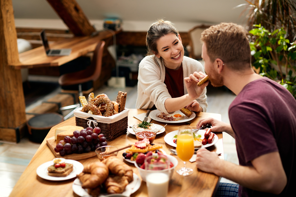 Happy couple enjoying in breakfast together at home. Focus is on woman feeding her boyfriend.