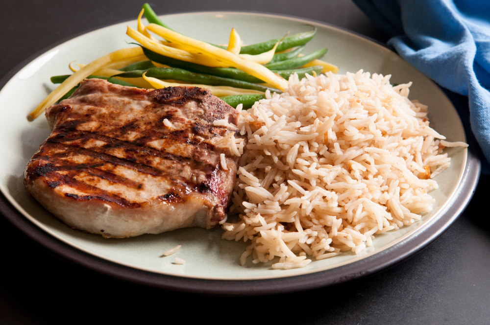A closeup shot of a grilled pork chop with rice and steam vegetables