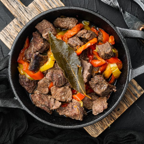 Kipovenschotel Hachee 8 schotels a 375 gram 1 Beef stew goulash - rustic style set, in cast iron frying pan, on black stone background, top view flat lay